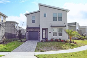 A modern two-story residential building with a garage, a well-maintained lawn, and a small palm tree.