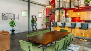 A spacious living area with a large wooden table and green chairs, a red spiral staircase, and a kitchen area with wooden cabinets and pendant lighting. - Unique; Modern; Spiral Staircase; Loft; Near IU; Whirlpool Tub; Natural Light (Bloomington)