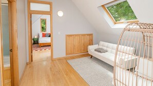 A room with a sloped ceiling, a white sofa, a wicker chair, a small window, and a door leading to another room. - Unique; Modern; Spiral Staircase; Loft; Near IU; Whirlpool Tub; Natural Light (Bloomington)