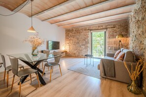 A modern living room with a glass dining table, grey chairs, a sofa, and a stone wall.