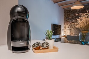A Krups coffee maker on a countertop with two coffee pods and a small potted plant.