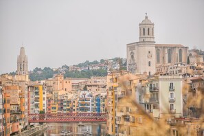 A cityscape with historic buildings, a prominent church with a bell tower, and a river reflecting the architecture. - Flateli. P.C 32 (Gerona / Girona)