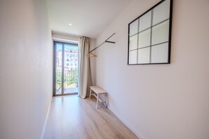 A hallway with a bench, a hanging coat rack, and a large window with a view of buildings.