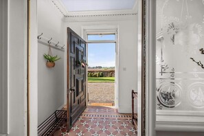 A hallway with a patterned floor, a dark wooden door, and a view of a green landscape through an open door. - The Farmhouse - Countryside Escape with Hot Tub (Kirkton of Monikie)