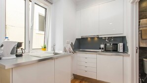 A modern kitchen with white cabinets, a microwave, a kettle, and a sink. - Hidden Gem in Alfama (Lisbon)