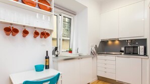 A compact kitchen with white cabinets, a microwave, and a window with a view. - Hidden Gem in Alfama (Lisbon)