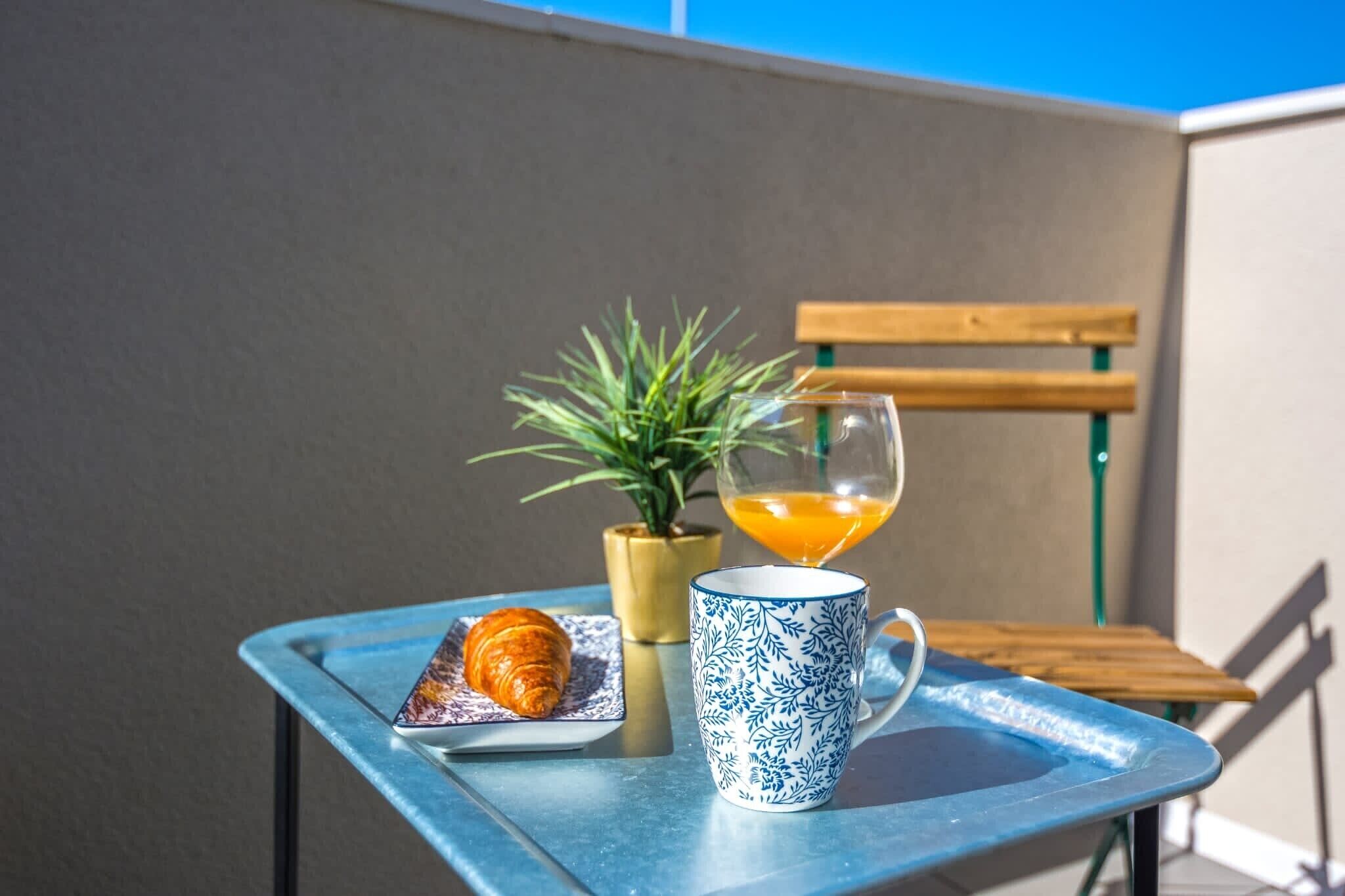 Una mesa con un croissant, un vaso de jugo de naranja y una taza azul y blanca con diseño.