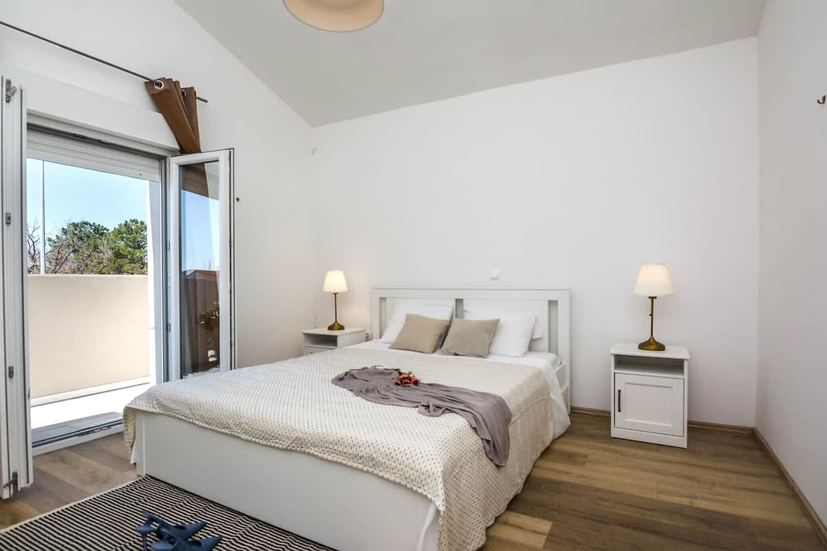 Ein Schlafzimmer mit einem Bett, zwei Nachttischen mit Lampen, einer Schiebetür zu einem Balkon und einer Deckenleuchte.