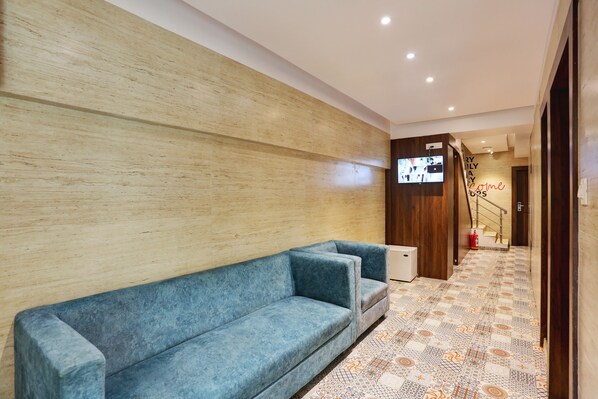 A modern lobby with a blue sofa, patterned carpet, wooden wall, and a staircase with a neon sign.