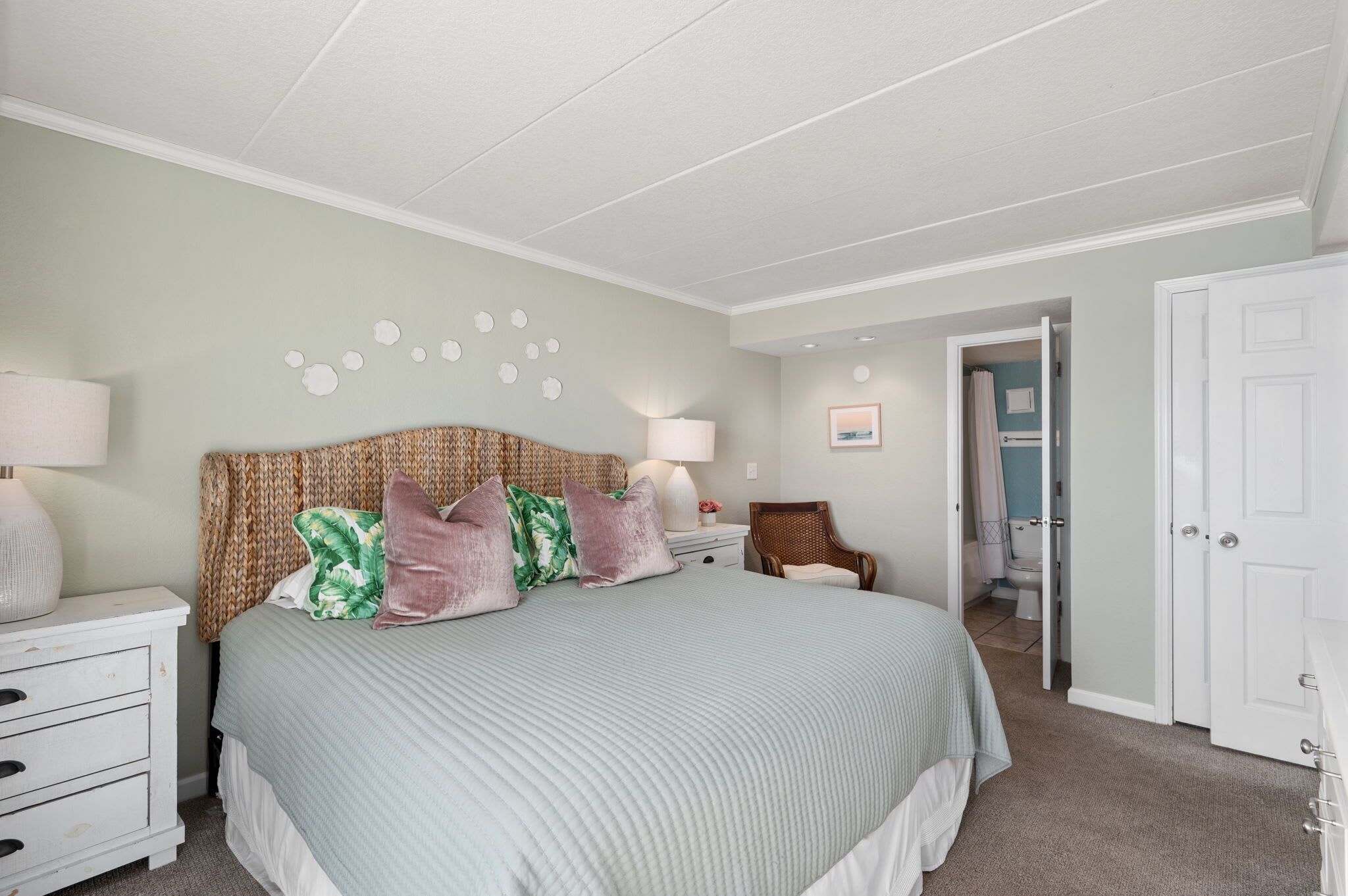 A bedroom with a bed, nightstands, a chair, and a door leading to a bathroom.