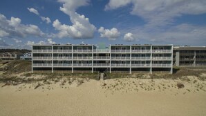 A multi-story hotel with balconies, located on a sandy beach with a clear sky. - Pup-Friendly! Direct Oceanfront! Shorely Goodness: PierView 105 Oceanfront Condo (Nags Head)