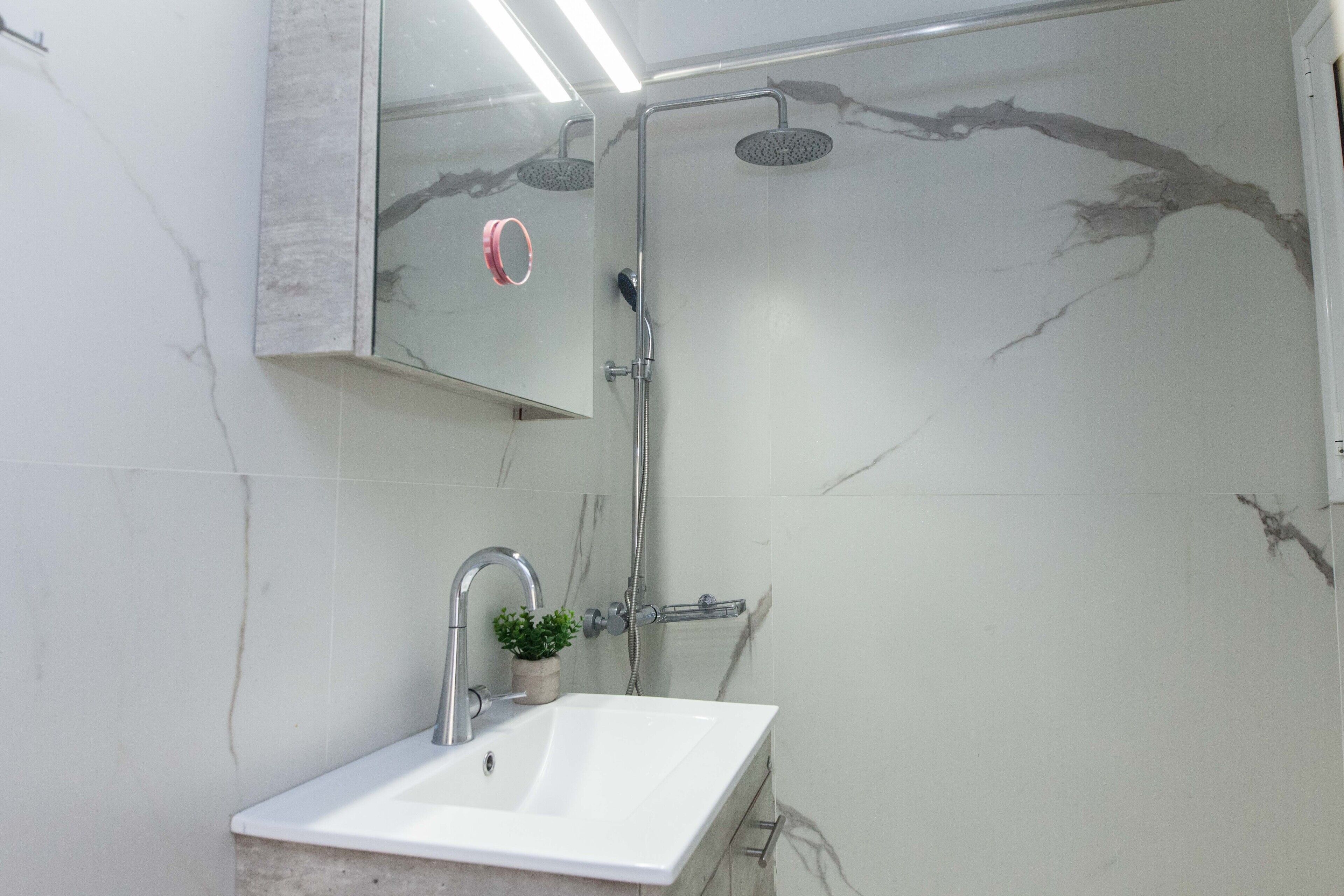 Een badkamer met een witte wasbak, een handdouche en een spiegel aan de muur.