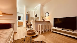 A modern living room with a sofa, a TV, a dining area with chairs, and a kitchen in the background.