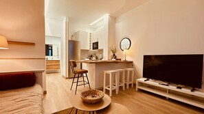 A modern living room with a sofa, a TV, a dining area with stools, and a kitchen in the background.