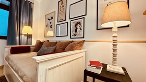 Une chambre à coucher avec un lit, des oreillers, une table de chevet avec des livres, une lampe et des tableaux encadrés accrochés au mur.