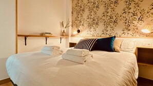 Una cama bien hecha con sábanas blancas, una almohada a rayas y una almohada azul. Hay dos toallas dobladas sobre la cama.
