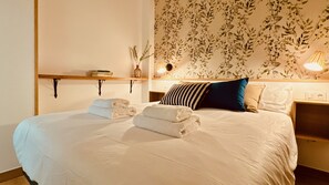 A neatly made bed with white linens, a striped pillow, and a blue pillow. There are two towels folded on the bed.