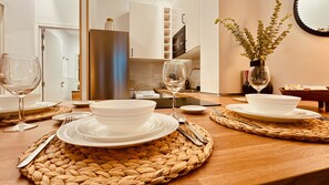 Une table à manger dressée avec de l’assiette, des bols et des couverts blancs, agrémentée de sets de table en fibres tressées et d’un vase rempli de verdure.