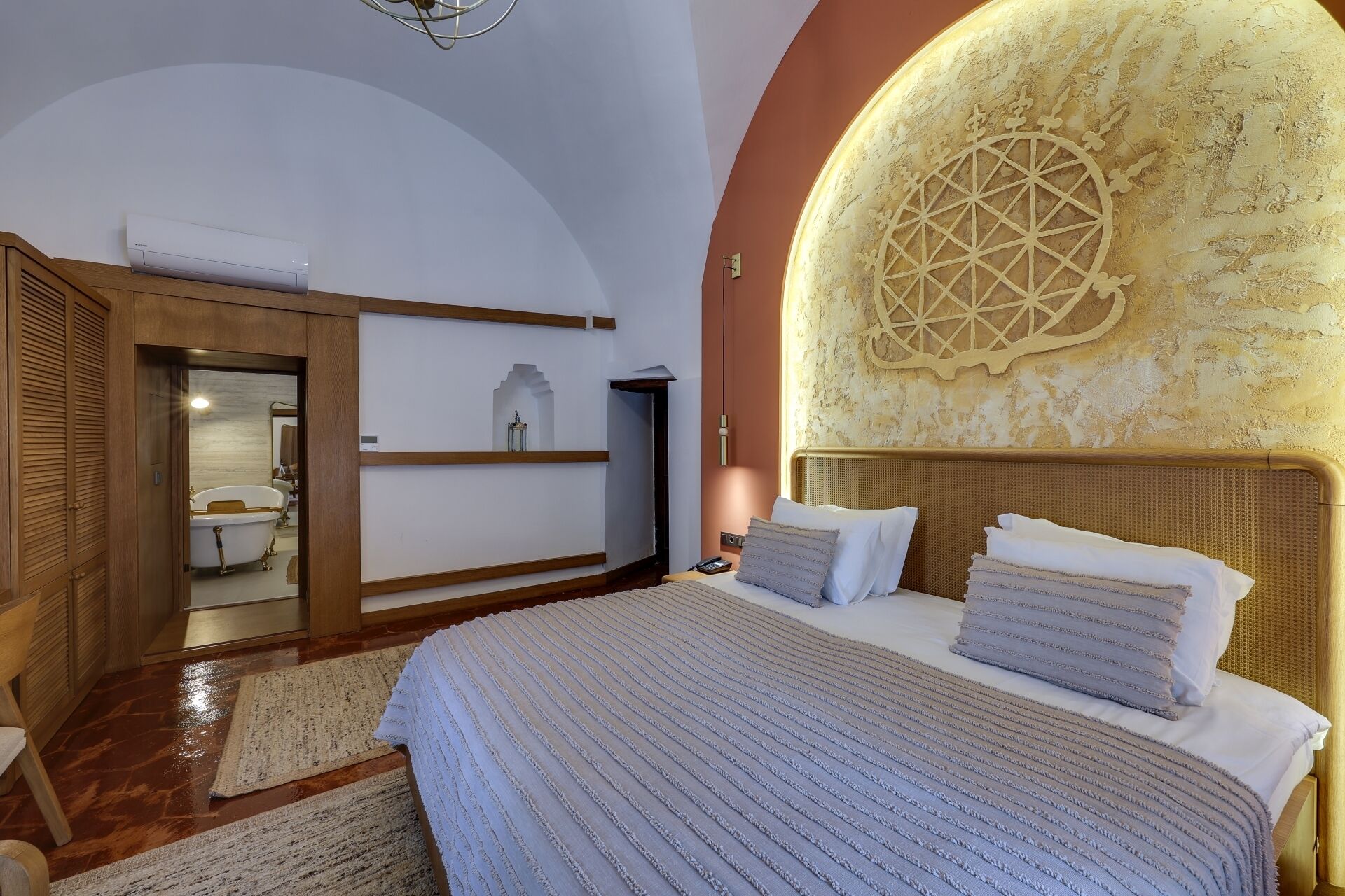 A bedroom with a large bed, a wooden wardrobe, a built-in bathtub, and a decorative wall.
