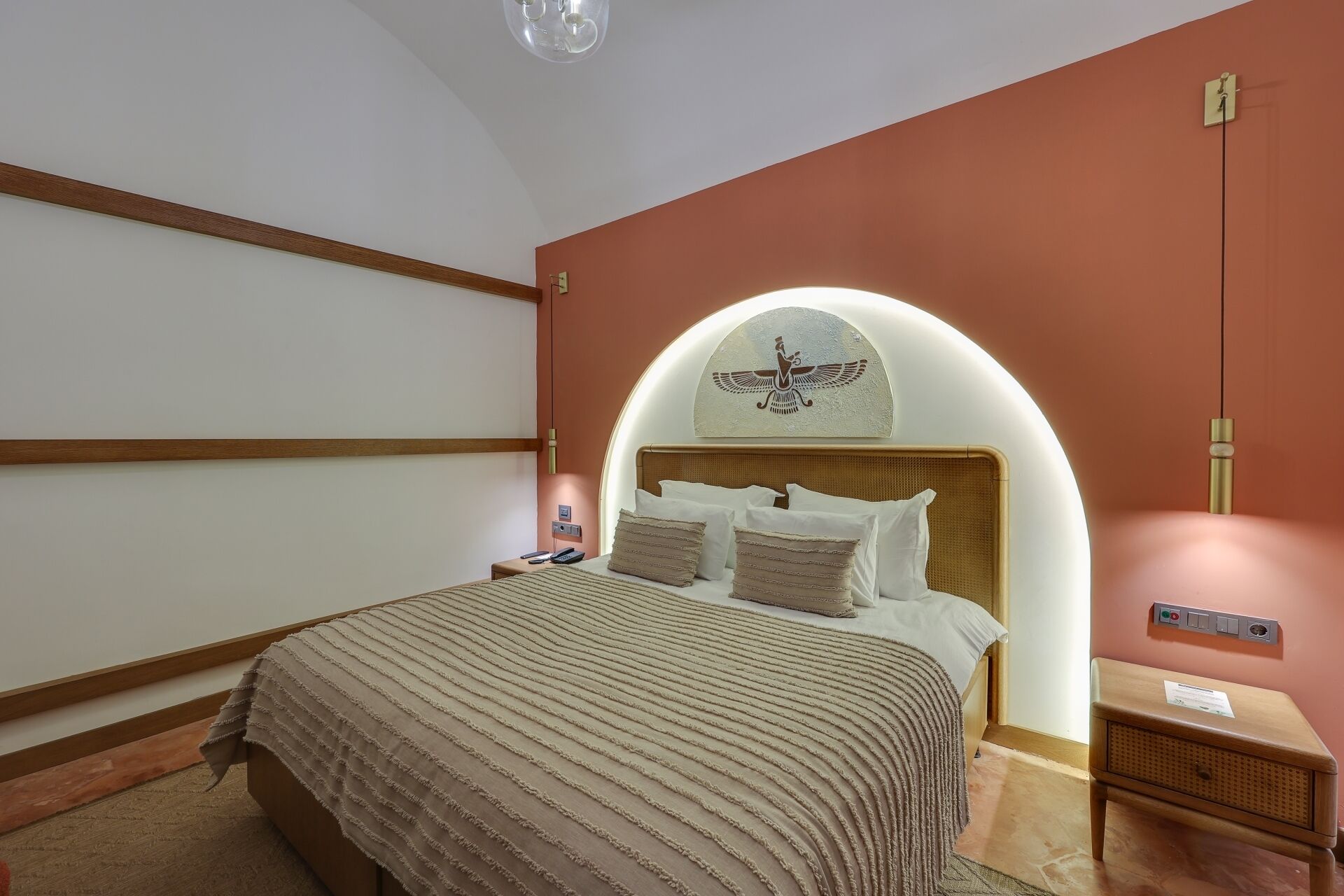 A bedroom with a bed, a nightstand, a wall-mounted light, and a decorative wall piece.