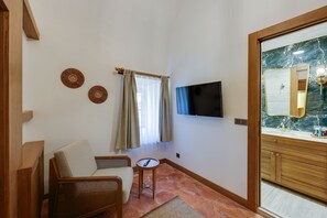 A living room with a flat-screen TV, two wicker chairs, a small round table, and a window with curtains. - Silk Road Museum Hotel (Tokat)