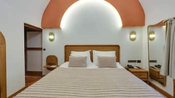 Hotelkamer met een groot bed, een houten hoofdbord, twee nachtkastjes, een spiegel en een wandlamp.