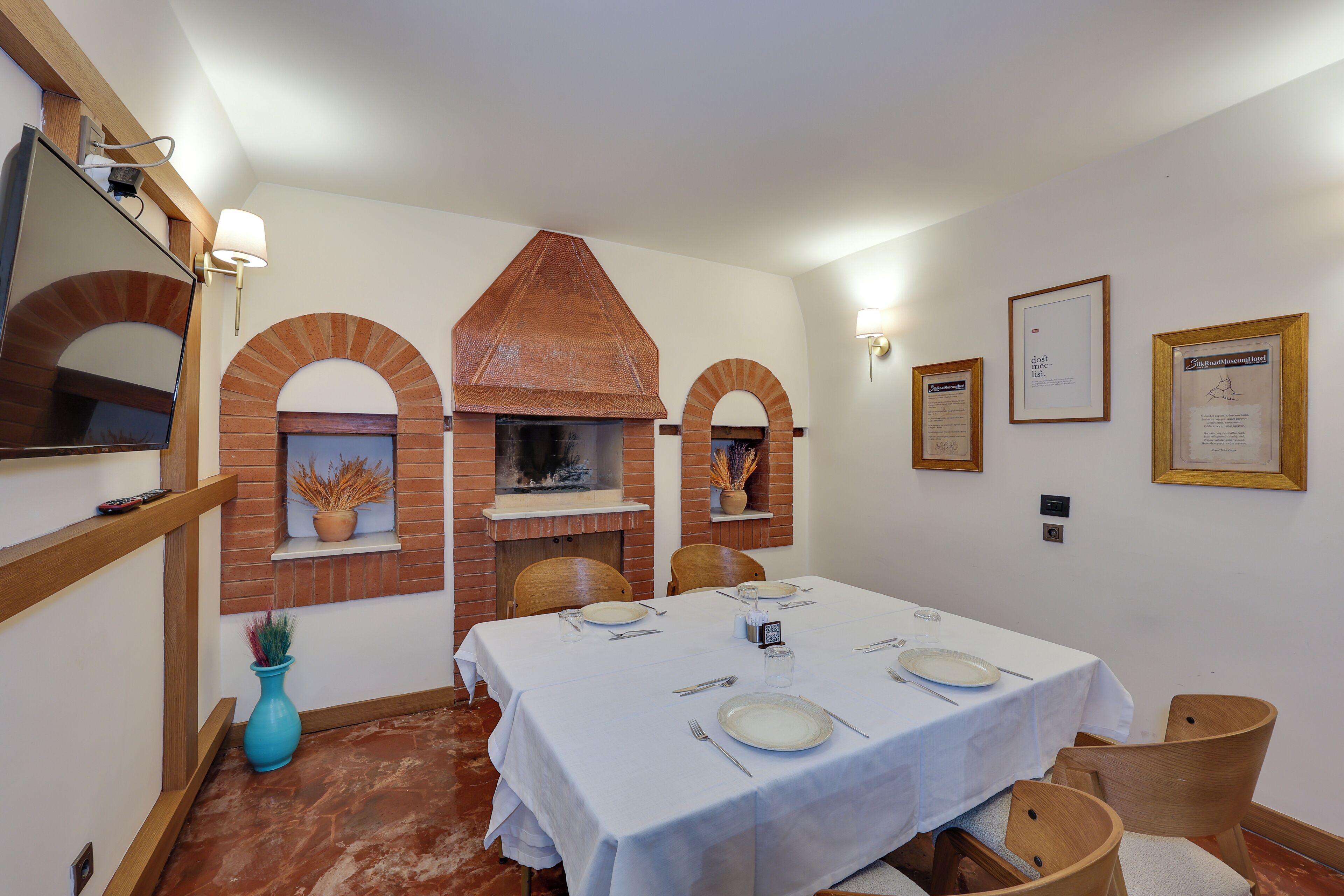 Comedor con chimenea de ladrillo, manteles blancos y sillas de madera.