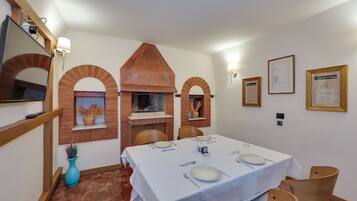 Comedor con chimenea de ladrillo, manteles blancos y sillas de madera.