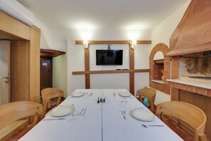 A dining area with a long table set for four, a television mounted on the wall, and a brick oven. - Silk Road Museum Hotel (Tokat)