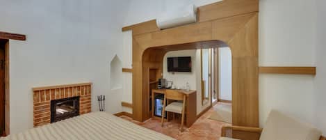 A bedroom with a fireplace, a bed, a desk with a chair, and a television.