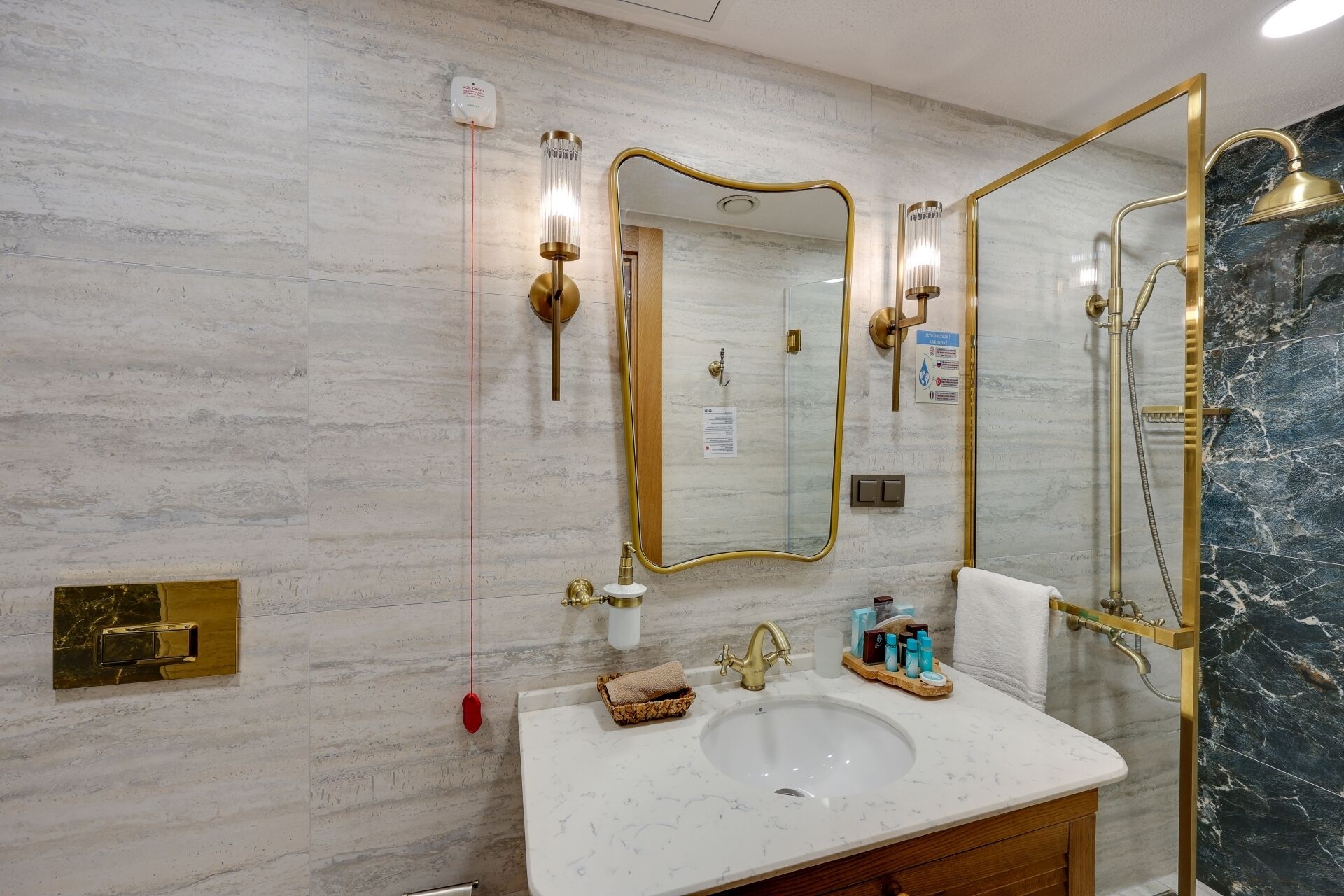 Un baño con lavamanos de mármol, detalles dorados y un espejo grande.