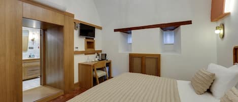 A bedroom with a bed, a desk, a television, a wardrobe, and a small window.