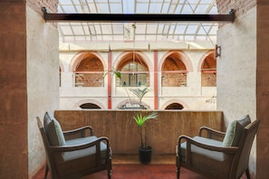 A balcony with two wicker chairs, a potted plant, and a view of a building with arched windows. - Silk Road Museum Hotel (Tokat)