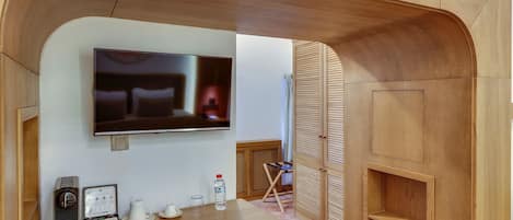 A modern room with a flat-screen TV mounted on the wall, a wooden desk with a Nintendo Switch, a water bottle, and a coffee maker.