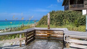 A wooden deck with a railing, overlooking a beach with clear turquoise water and a building with a balcony. - 30A Gem | Rooftop Patio | Heated Pool (Santa Rosa Beach)