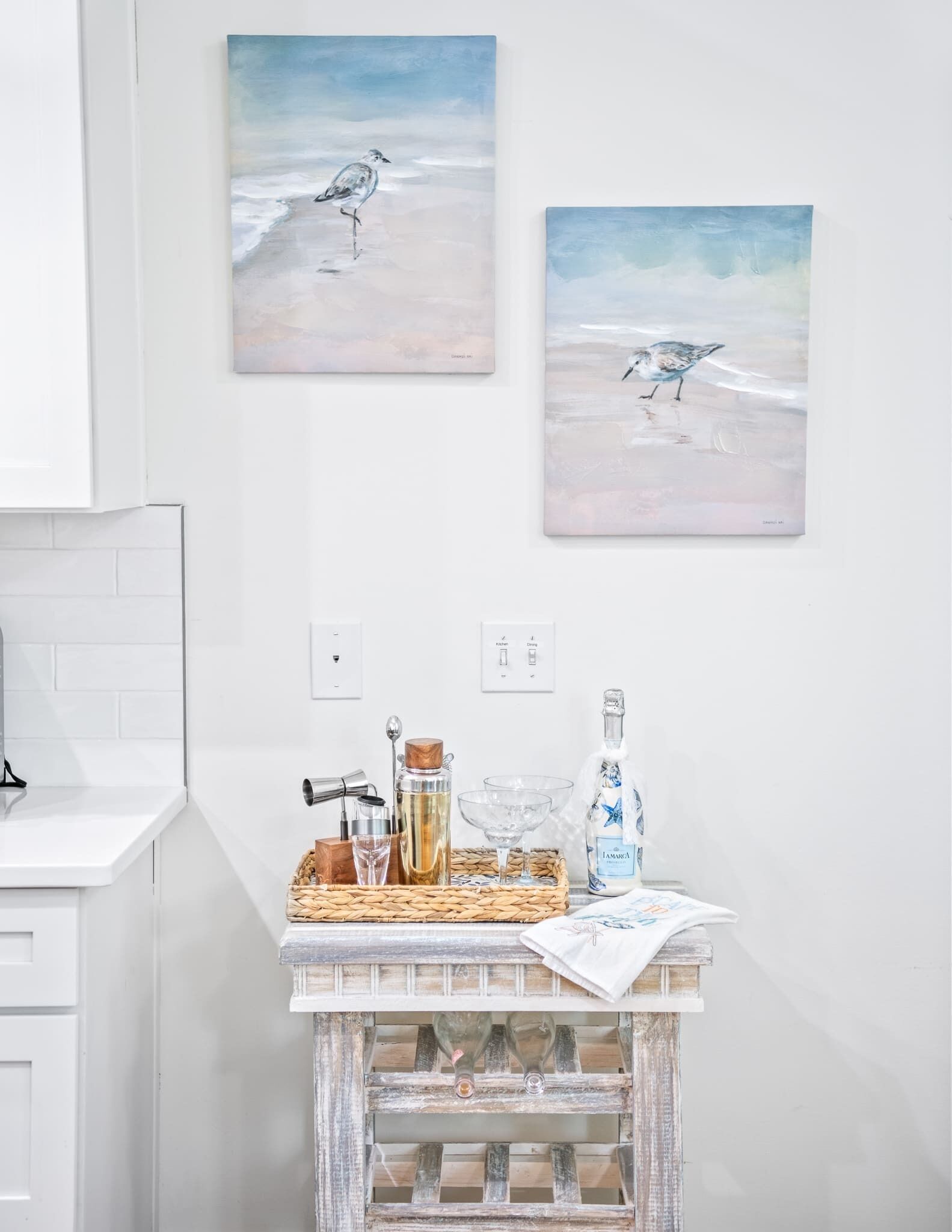 A kitchen with white cabinets, a white countertop, and two seagull paintings on the wall.