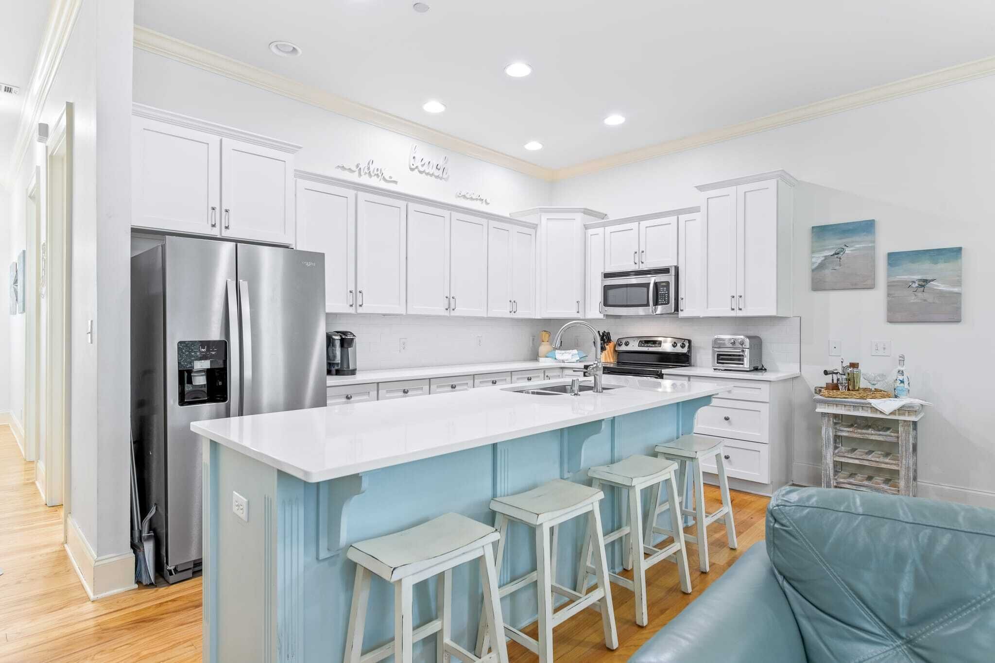 A modern kitchen with white cabinets, a stainless steel refrigerator, a microwave, and a large island with bar stools.