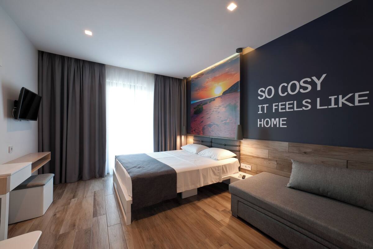 A modern hotel room with a bed, a sofa, a desk, and a TV.