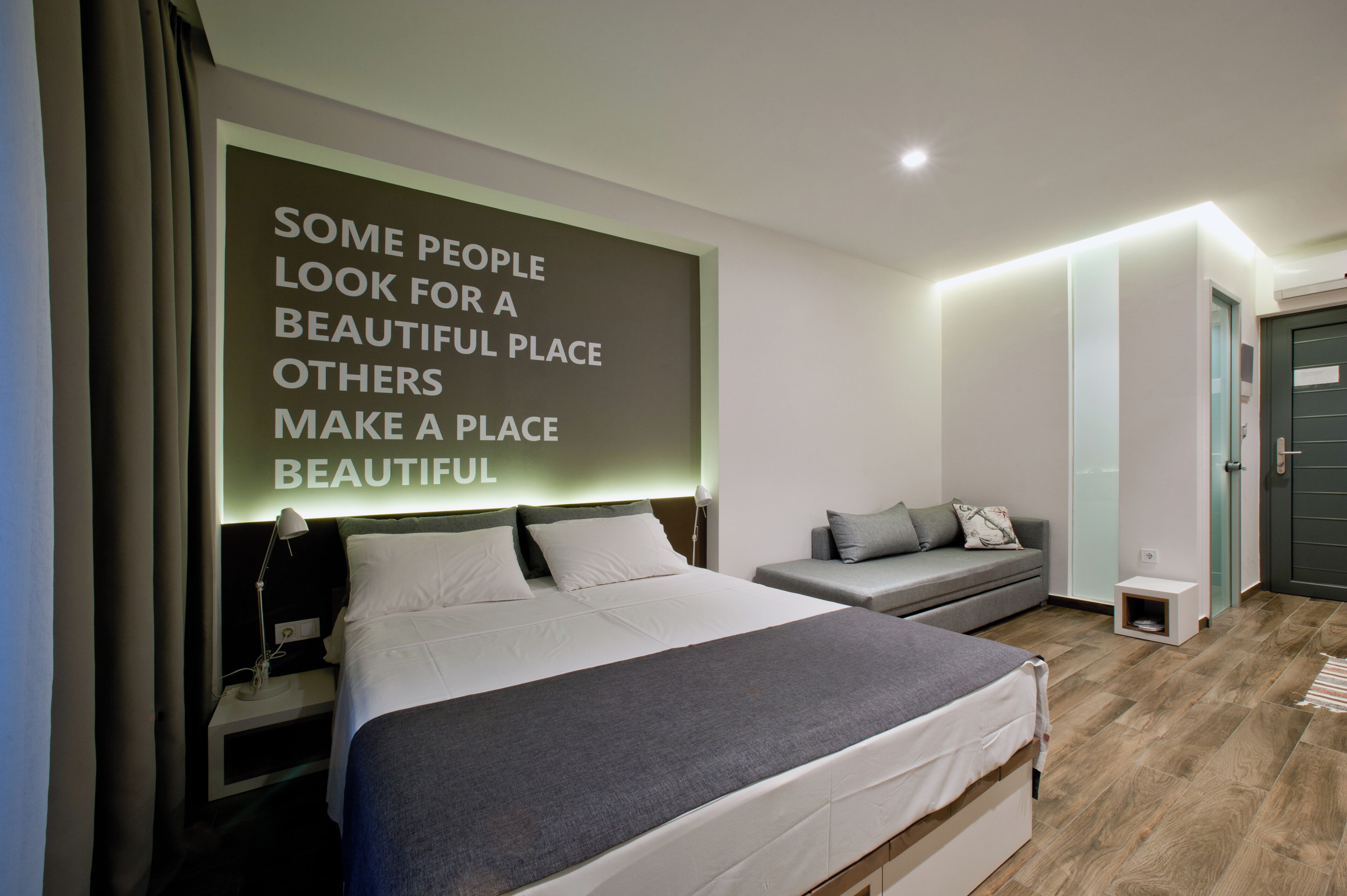 A modern bedroom with a large bed, a bedside table, a small seating area, and a motivational quote on the wall.
