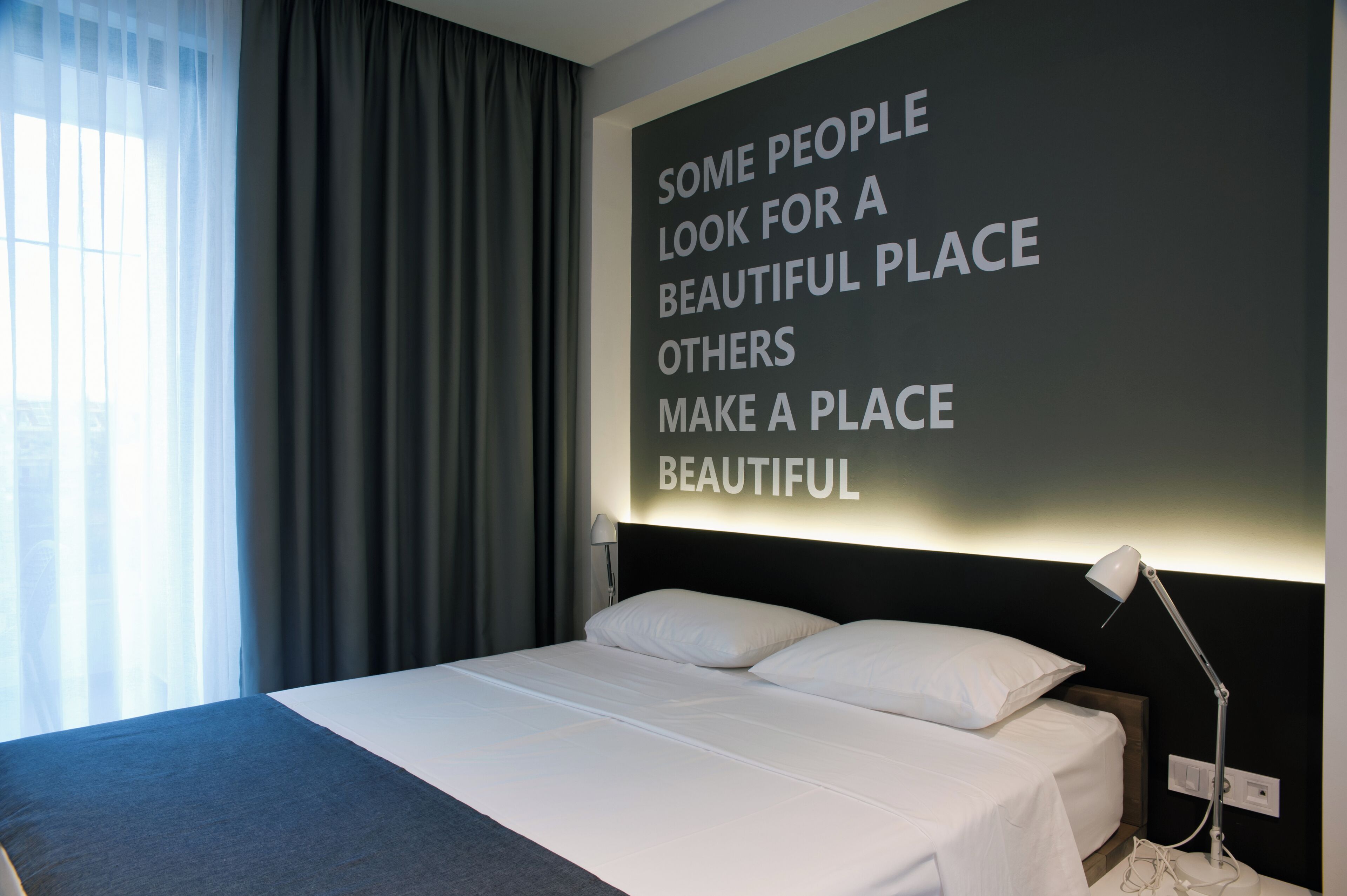 Una habitación de hotel moderna con una cama grande, una lámpara de noche y una cita motivacional en la pared.