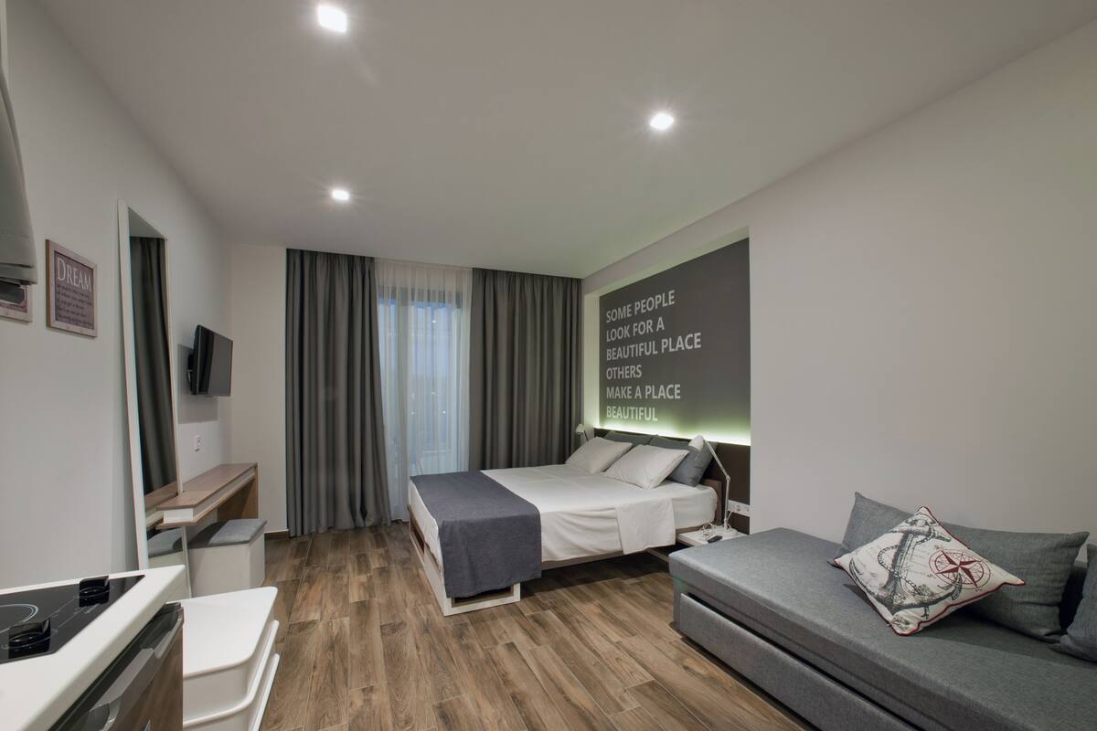 A modern hotel room with a bed, a desk, a sofa, and a wall-mounted TV.