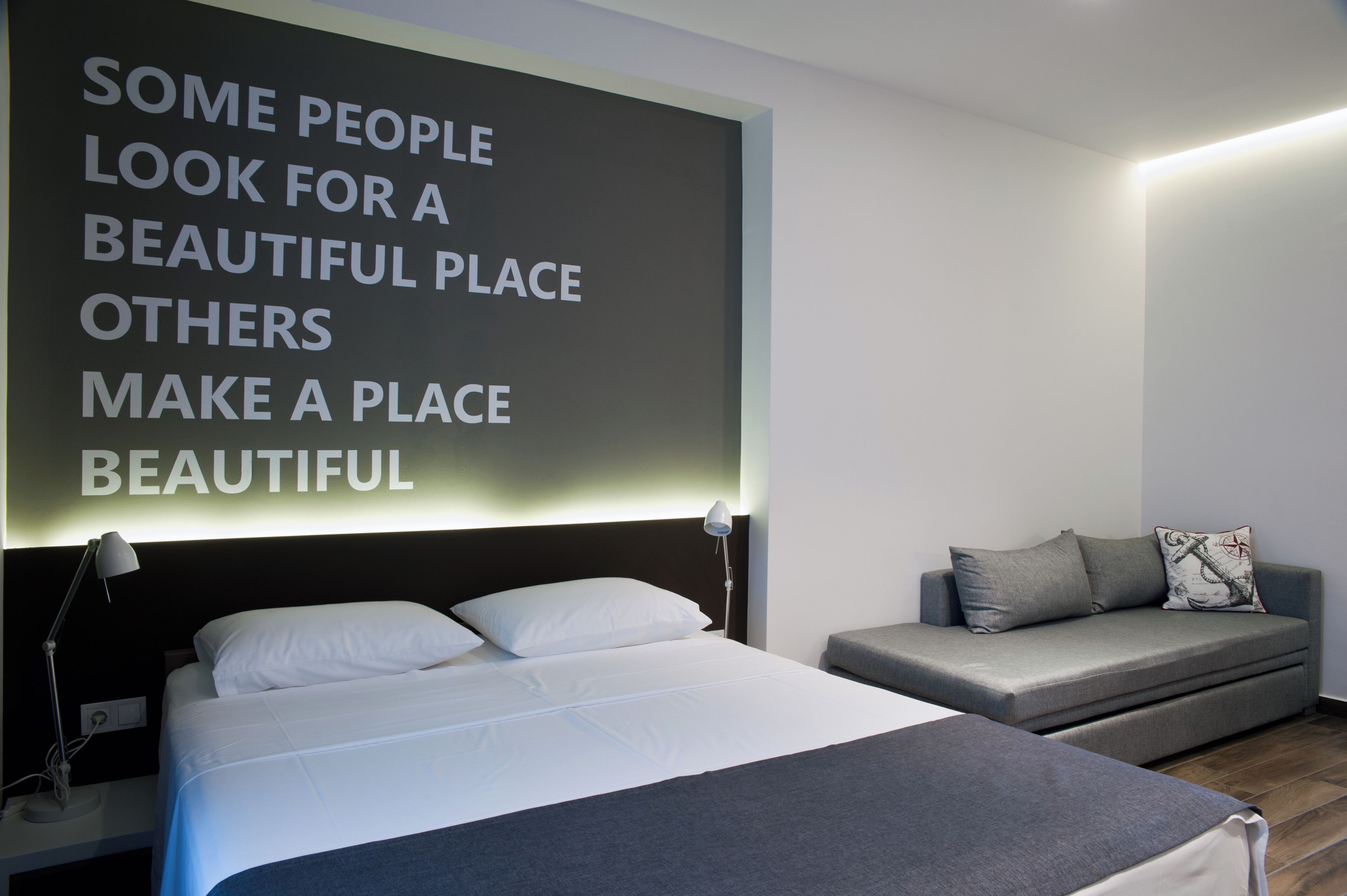 A modern bedroom with a large bed, a sofa, and a motivational quote on the wall.