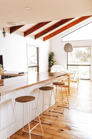 Cocina moderna con vigas de madera, una encimera larga y taburetes de bar.
