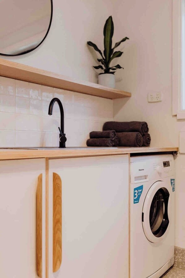 Una cocina compacta con lavadora, tiradores de madera en los armarios y una planta en maceta sobre la encimera.