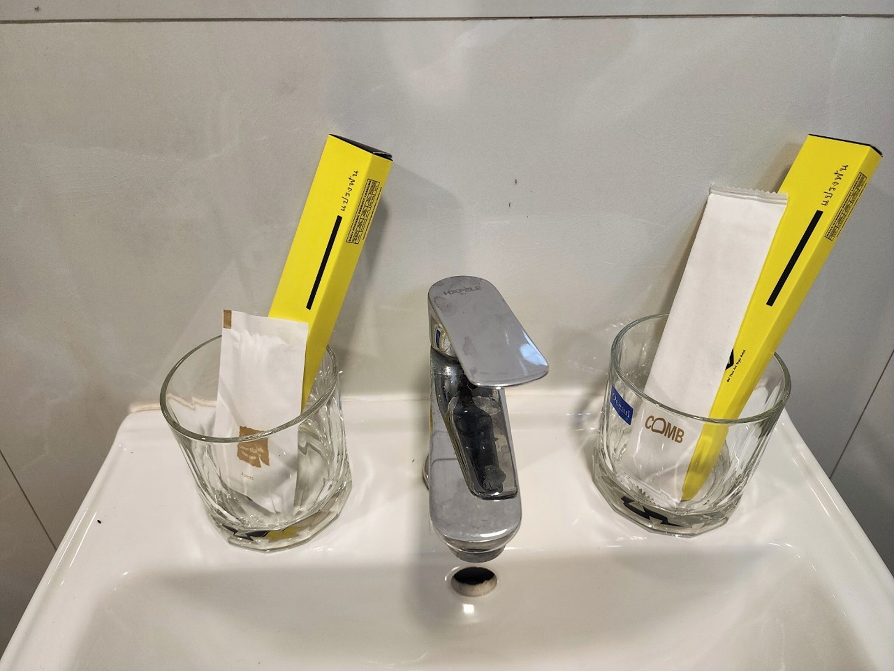 Un lavabo de salle de bain avec deux verres en verre contenant des mouchoirs et un robinet argenté.