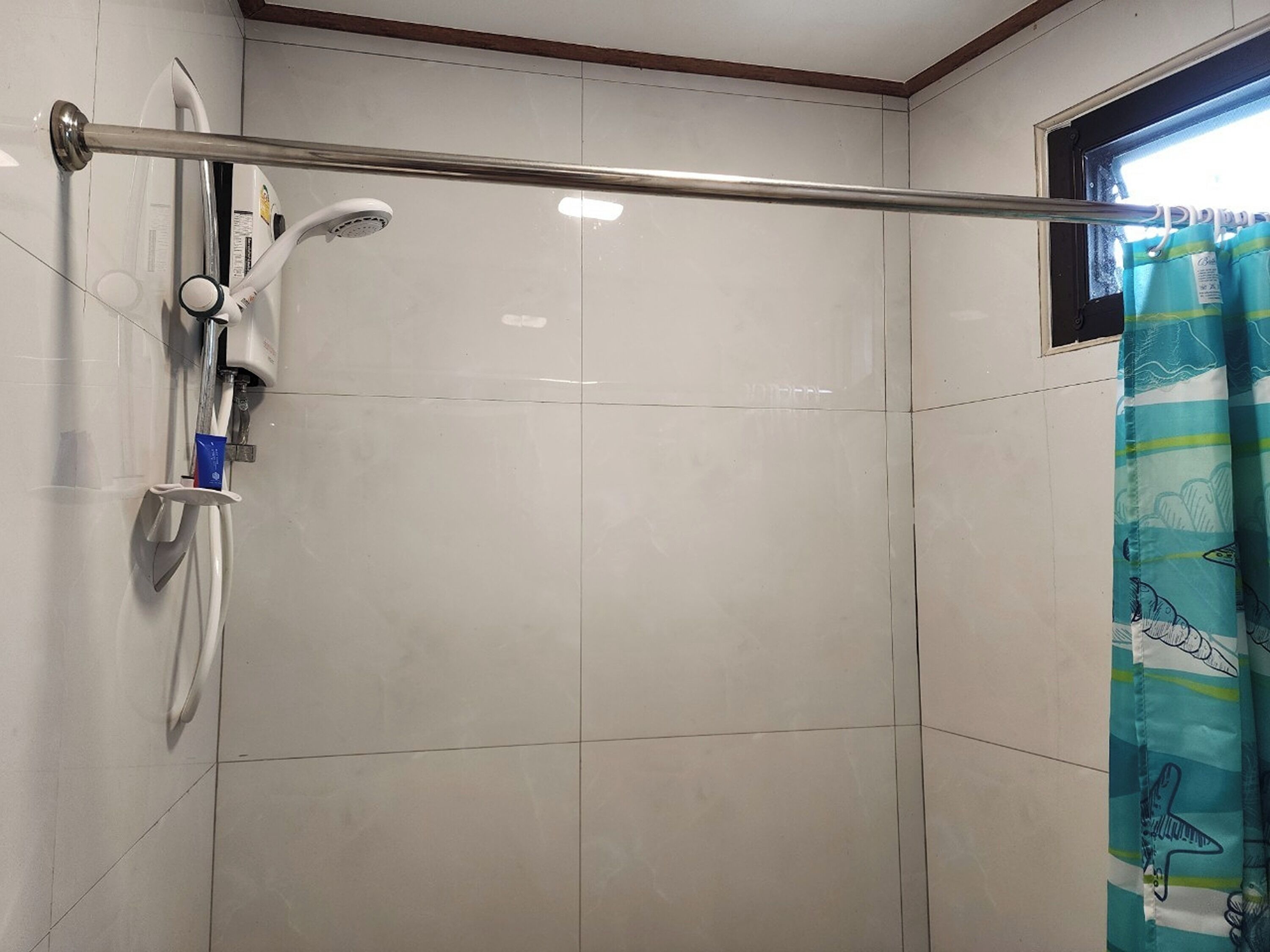 A bathroom with a shower, a hand dryer, and a window with a curtain.