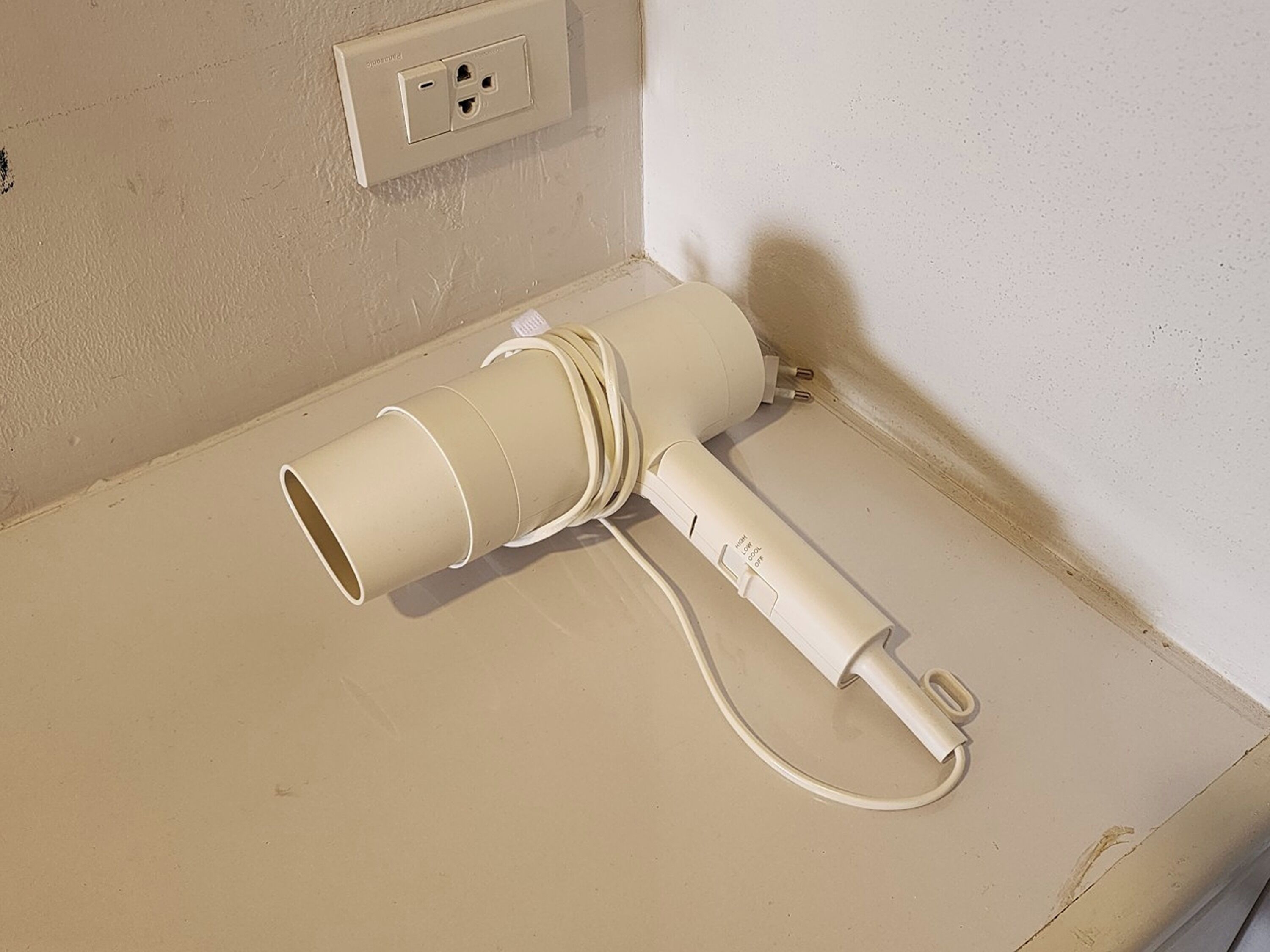 Un secador blanco sobre una encimera color beige, junto a un enchufe de pared.