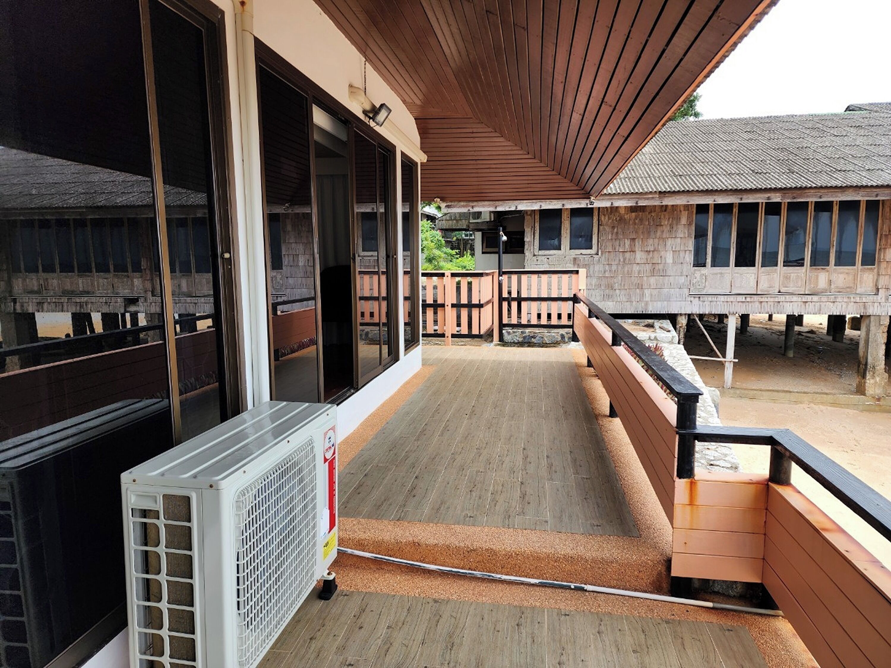Un balcon doté d’un plancher en bois, d’un climatiseur blanc et offrant une vue sur un bâtiment traditionnel avec un toit en tuiles.