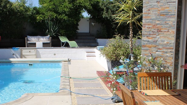 Eine Holzterrasse mit Pool, Gartenmöbeln und einer Steinmauer.