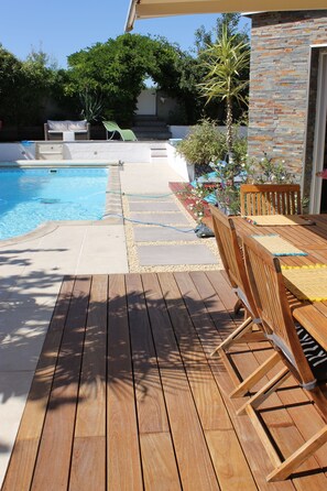 A wooden deck with a pool, outdoor furniture, and a stone wall. - Belle Maison Tout Confort Avec Piscine, Clim, sal de Sport, Sauna,10 min de St (Breuschwickersheim)
